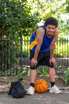 Man pausing on park path, leaning forward, wearing blue yellow jersey, backpack 스톡 사진