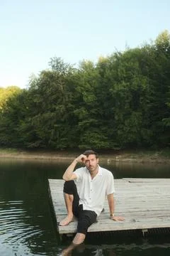 A man is peacefully sitting on a dock overlooking a serene lake Stock Photos