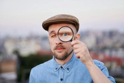 Man in peaked cap looking at camera using magnifying glass Stock-Fotos