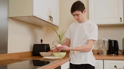 Man peeling boiled egg in kitchen. Male preparing food while holding egg over Stock Footage 303064146