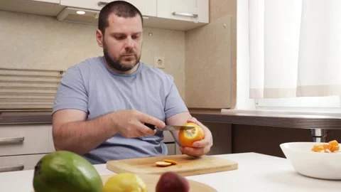 Man peeling an orange in the kitchen, middle-aged Caucasian person, healthy.. Stock Footage 310828593
