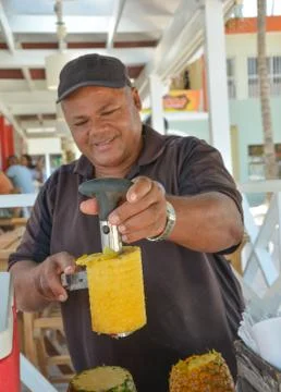 Man peeling a pineapple with a cutter. Focus on the hand holding the pineappl Stock Photos