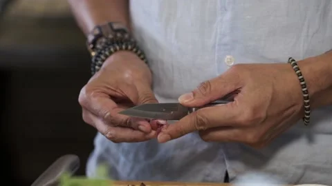 A man is peeling shallots with a small knife wearing a blue shirt Stock Footage 145355148