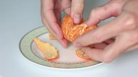 Man peeling a tangerine on a white surface Stock Footage 71954153