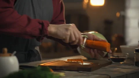 Man peels carrots in a cozy kitchen setting while preparing a healthy meal Stock Footage 331354787