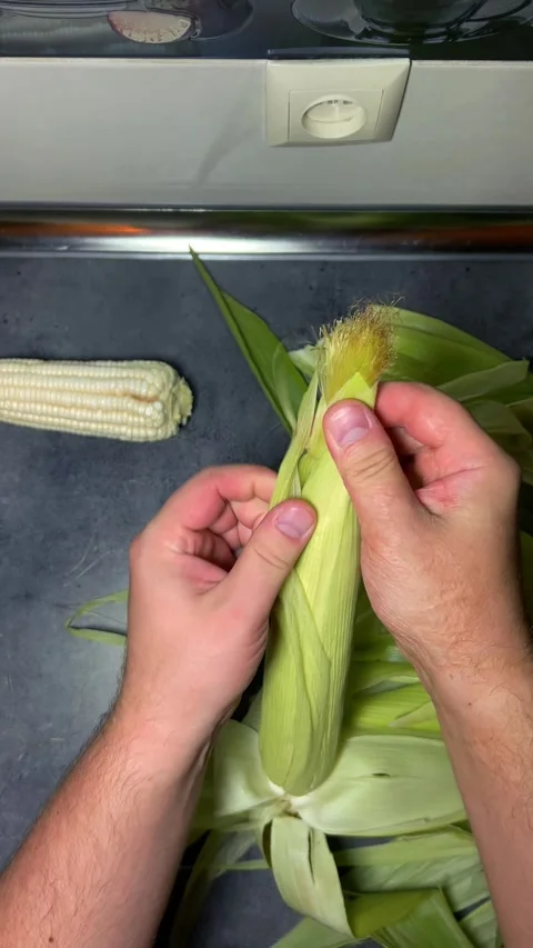 Man peels fresh raw cob of corn on gray kitchen table. POV Stock Footage 282688911