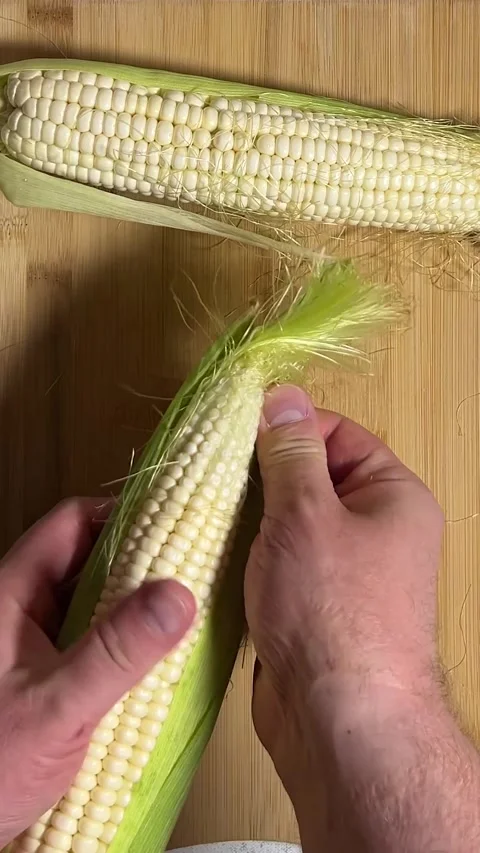 Man peels fresh raw cob of corn on wooden cutting board on kitchen table Stock Footage 282841341