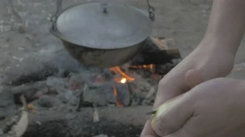 A man peels potatoes on the background of a campfire in the evening Video stock 135839073