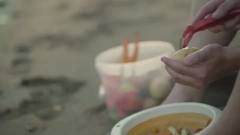 Man peels potatoes while sitting on the sand. Stock Footage 142189270