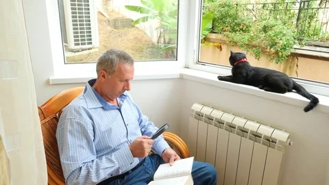 A man a pensioner reads a book through a magnifying glass at home by the window Stock Footage 80331808