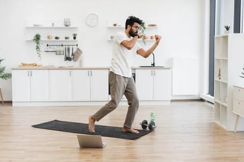 Man performing boxing-style workout in modern kitchen setting with laptop on mat Stock Photos