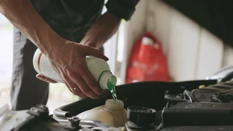 Man performing car maintenance by pouring fluid into the engine compartment in a Stock Footage 303806533