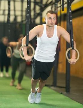 Man performing chest push-ups with gymnastic rings during workout in gym Stock Photos