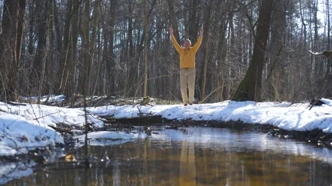 Man performing jumping exercise in winter forest near stream Vidéo 334371215