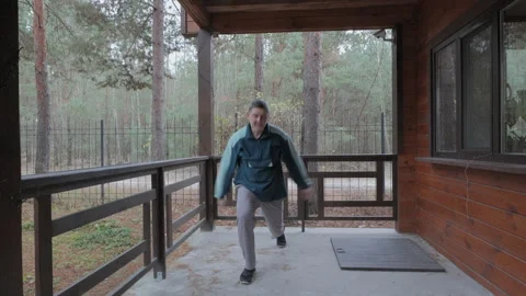 Man performing jumping jacks on wooden porch outdoors Stock Footage 335444863