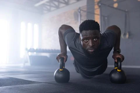 Man performing kettlebell push-ups gripping handles on rubber floor at gym Stock Photos