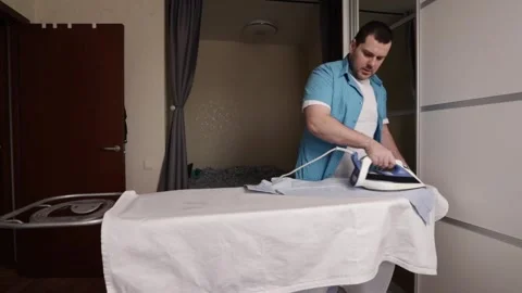 Man Performing Laundry Task While Ironing Shirt on Board at Home, Domestic .. Stock Footage 306531064