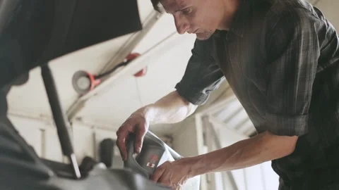 Man performing maintenance on a car engine in a garage during the daytime while Stock Footage 303805216