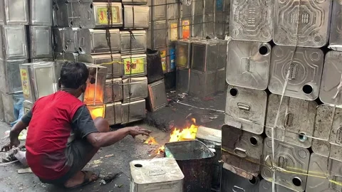 A man performing manual labor with fire near metal containers Video stock 306684079