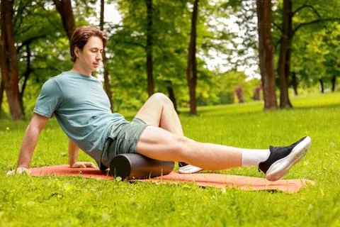 Man performing myofascial release using a foam roller on a mat in a park. S.. Foto stock
