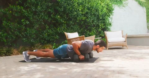 Man performing plank push-ups and single-arm hex dumbbell rows on patio mat, Stock Footage 339321208