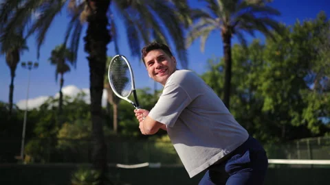 Man performing powerful tennis backhand on outdoor court with palm trees Video stock 325041781