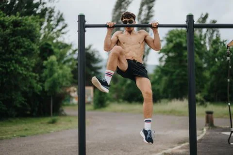 Man performing pull-ups on metal parallel bars in outdoor park Stock-Fotos