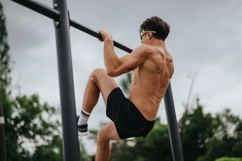Man performing pull-ups on outdoor gym equipment for strength training and Fotos Stock