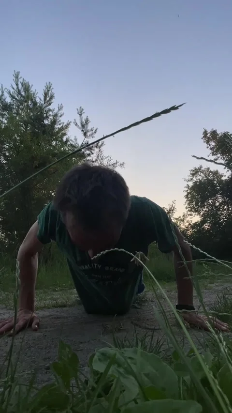 Man performing push-up outdoors from extreme low-angle during twilight, with Видео 344585357