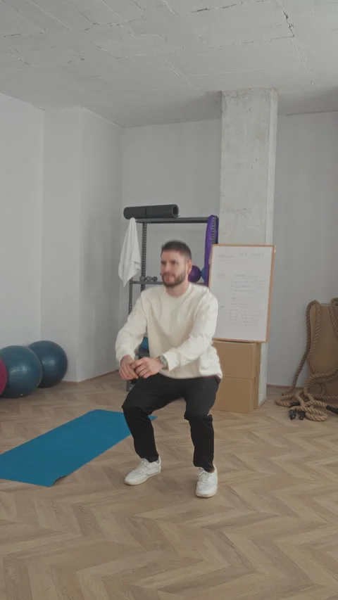 Man performing squat with hands extended on blue yoga mat in a fitness stud.. Stock Footage 337361961
