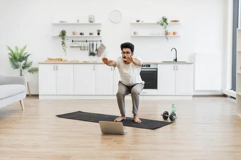 Man performing squats at home using online fitness video guidance Stock Photos