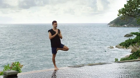 Man performing tree pose at infinity pool Stock Footage 74778868