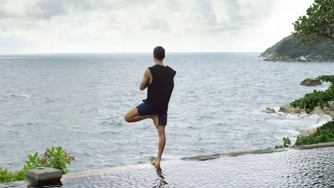 Man performing tree pose at infinity pool Stock Footage 74778963