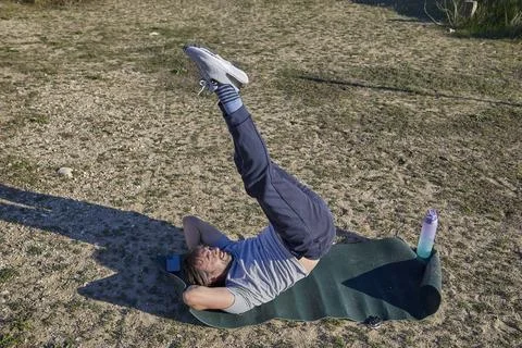 A man performing a vertical leg raise while lying on a fitness mat Stock Photos