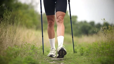 Man performing walking lunge warm-up with trekking poles on grassy nature trail Stock Footage 313951312