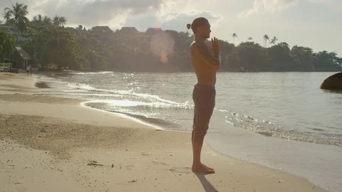 Man performing a warrior pose on beach during sunset Stock Footage 74773093
