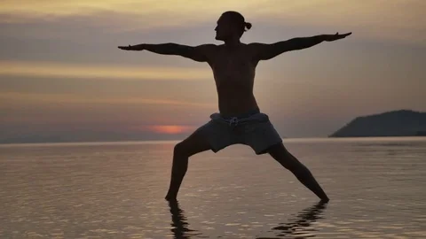 Man performing warrior pose during sunset on the beach Stock Footage 75288047