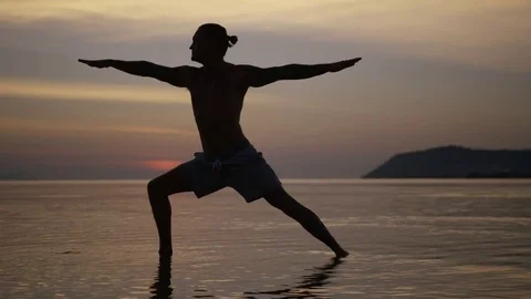 Man performing a warrior pose in the sea during sunset Stock Footage 74769672