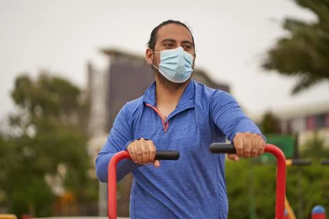 Man performs arm exercises on machinery in public square. use of mask in new  Stock Photos