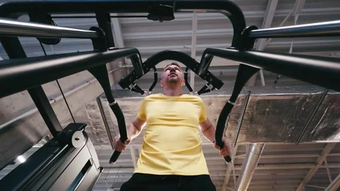 Man Performs Assisted Dips On Parallel Bars In Gym, Legs Supported Stock Footage 323390832