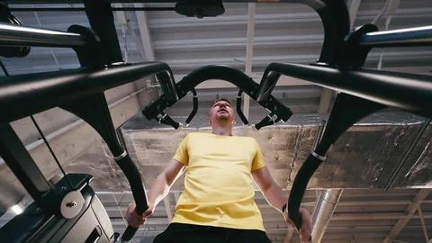 Man Performs Assisted Dips On Parallel Bars In Gym, Legs Supported Foto stock