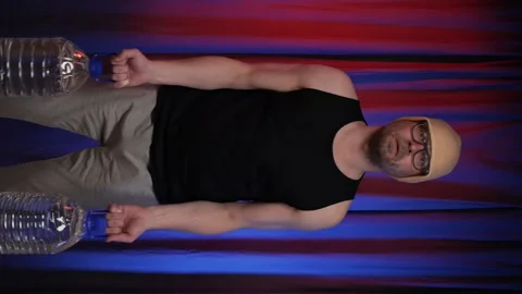 Man performs Bicep curls using two large bottles of water as a weight. Video stock 134914758