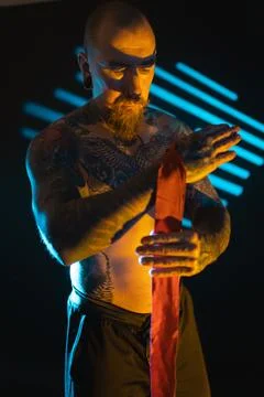 Man performs a dance routine with a red ribbon in a dark studio with blue and Stock Photos