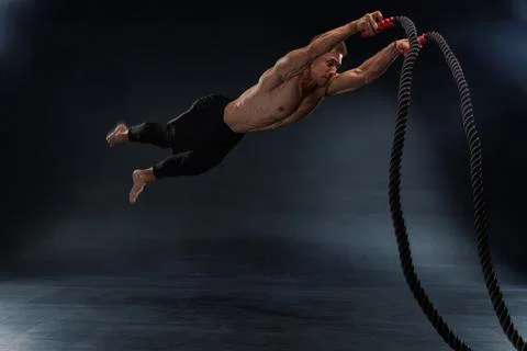 Man performs dynamic fitness exercise with battle ropes in a dark training Stock Photos