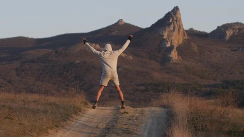 Man performs exercise on country road amid mountains in sunset Stock Footage 128742226