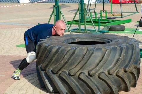 Man performs Exercise Tire Turning during strength competition Stock Photos