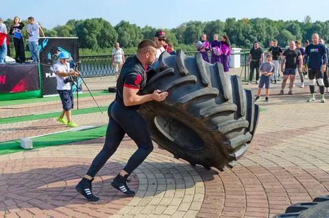 Man performs Exercise Tire Turning during strength competition Stock Photos