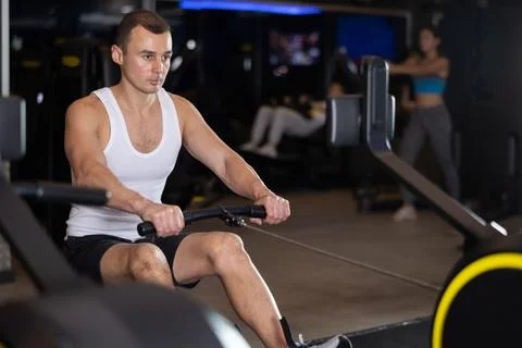 Man performs exercises with rowing machine in gym Photos