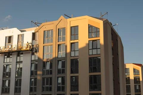 A man performs facade work from a suspended construction platform on a high-r Stock Photos