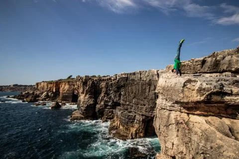 Man performs a handstand on the edge of cliff. Concept of extreme, freedom and Stock Photos